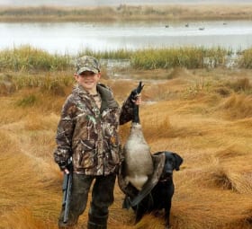 Very young hunter holding his kill beside his dog